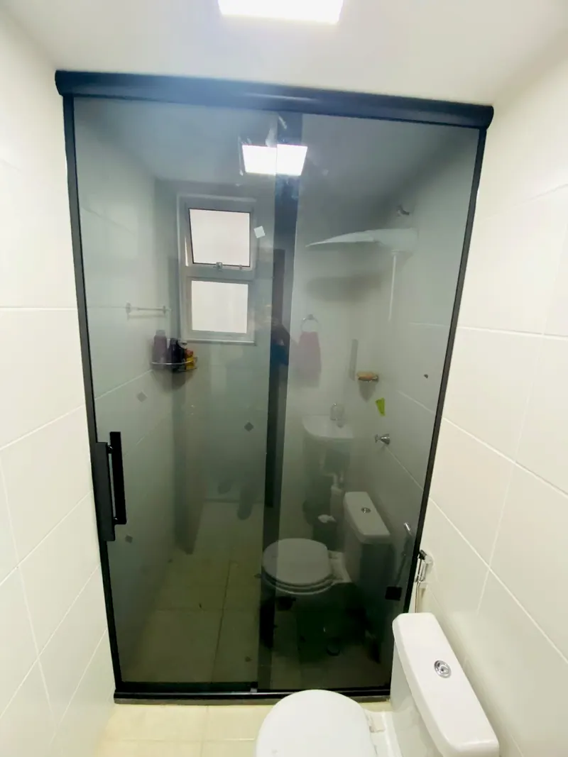 Box de correr em vidro fumê com perfil preto, num banheiro de azulejo branco